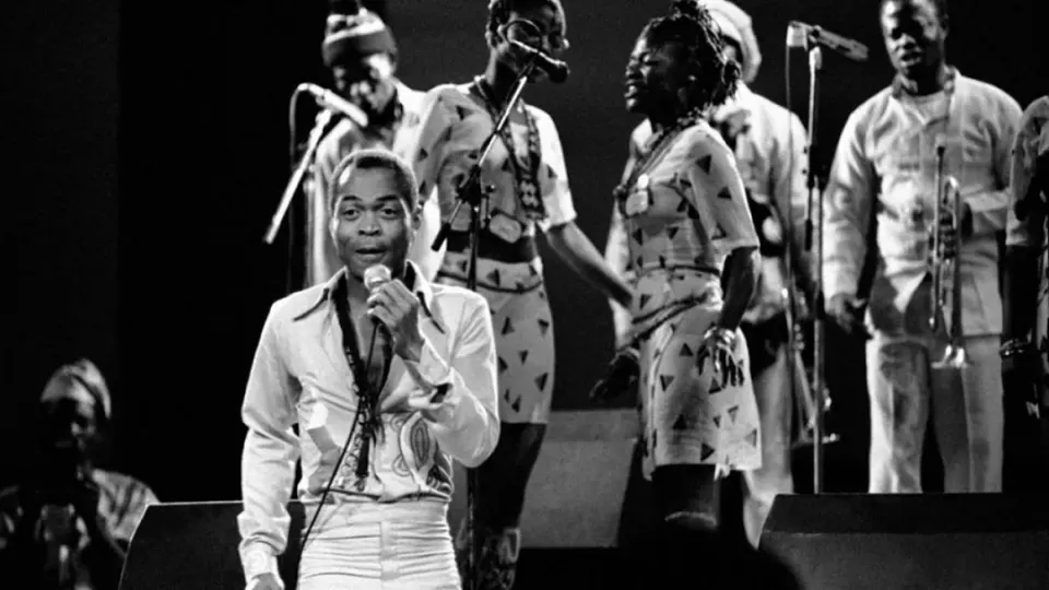 Fela Kuti singt am Mikrofon bei einem Konzert, hinter ihm seine Tänzerinnen und Musiker. Internet